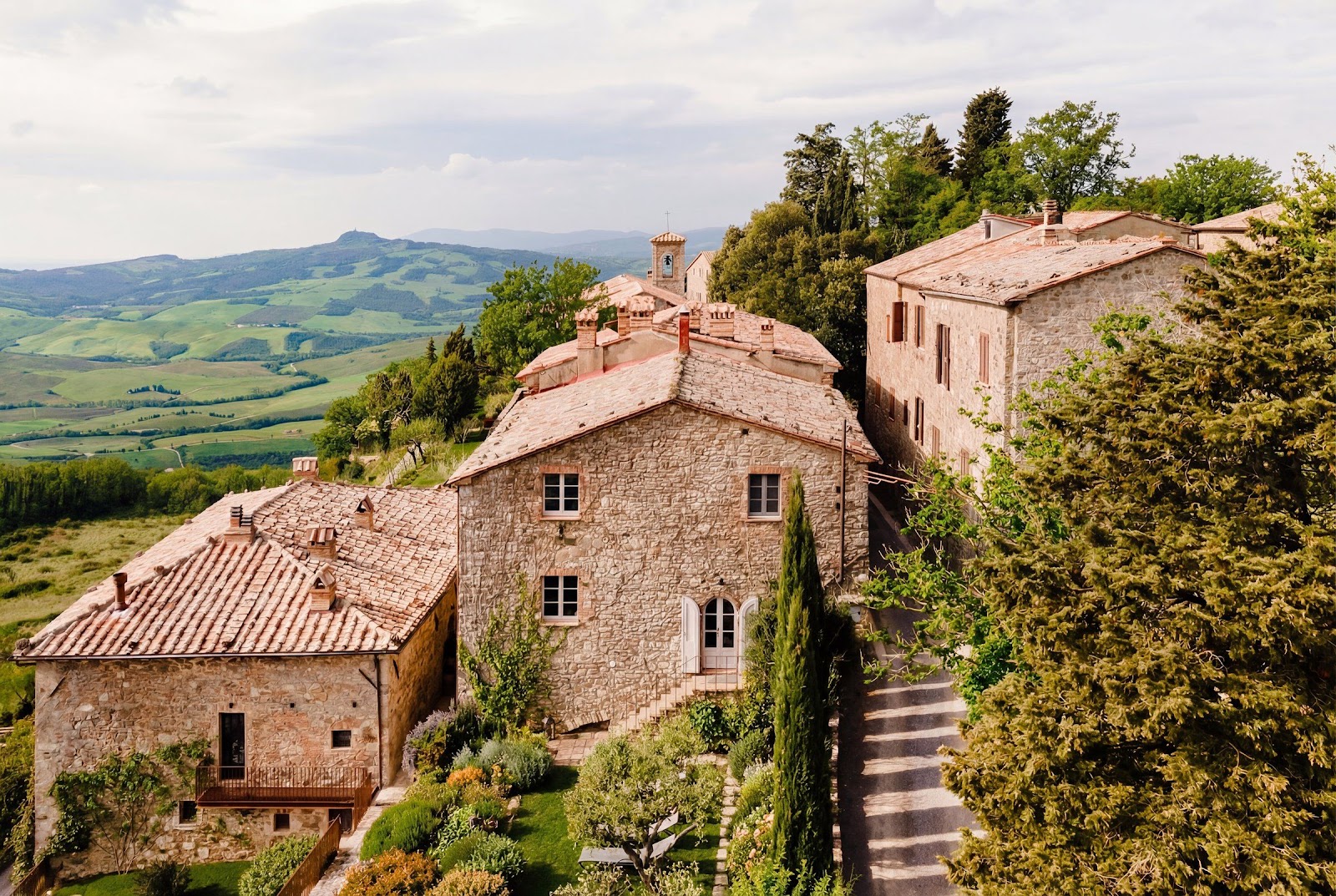 A stone house at the edge of a Tuscan hill village with the Val d&rsquo;Orcia countryside falling away behind it